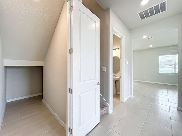 corridor featuring vaulted ceiling, light tile patterned flooring, and a textured ceiling