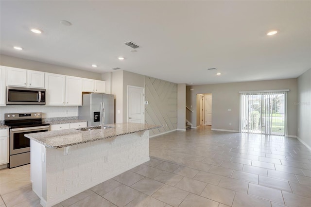 kitchen featuring stainless steel appliances, white cabinets, light stone counters, a breakfast bar area, and a kitchen island with sink