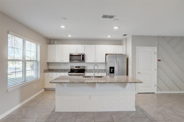 kitchen featuring an island with sink, stainless steel appliances, sink, light stone countertops, and white cabinets