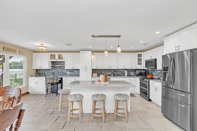 kitchen with a center island, a kitchen bar, pendant lighting, white cabinetry, and appliances with stainless steel finishes