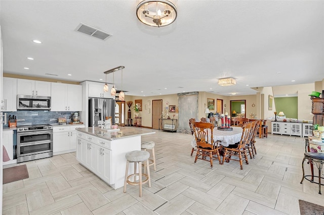 kitchen with stainless steel appliances, a breakfast bar, a center island, decorative light fixtures, and white cabinets