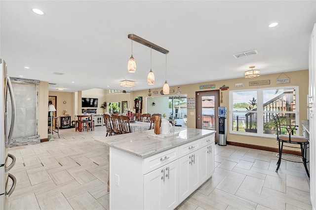 kitchen with a kitchen island, stainless steel fridge, white cabinetry, hanging light fixtures, and light stone counters