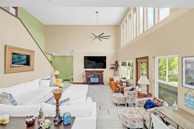 living room with ceiling fan, a fireplace, a towering ceiling, and light parquet floors