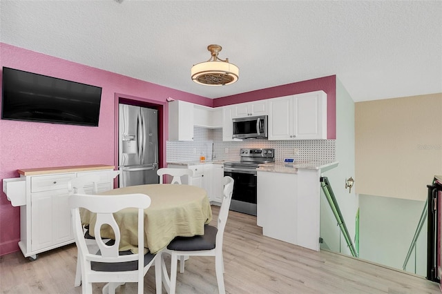 kitchen featuring appliances with stainless steel finishes, tasteful backsplash, white cabinetry, and light hardwood / wood-style floors