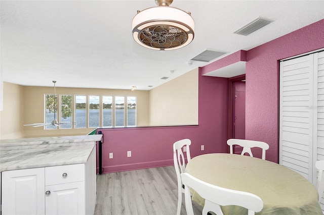 dining area with light hardwood / wood-style floors, a textured ceiling, and a water view