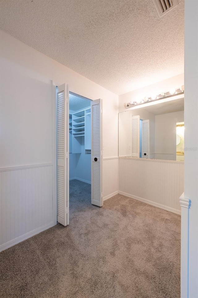 unfurnished bedroom featuring carpet, a spacious closet, a textured ceiling, and a closet