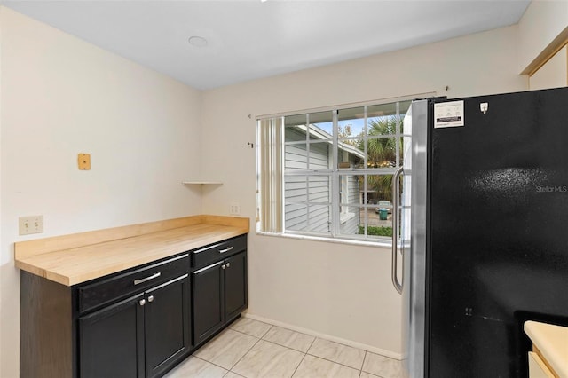 kitchen with stainless steel refrigerator, light tile patterned floors, and butcher block countertops