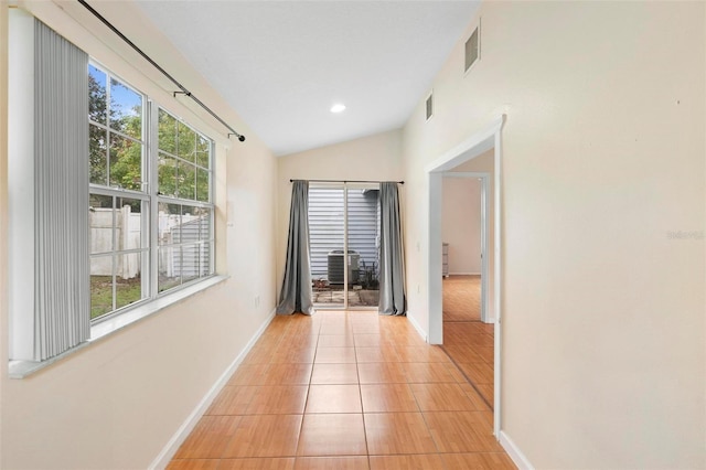 hall with a wealth of natural light, lofted ceiling, and light tile patterned flooring