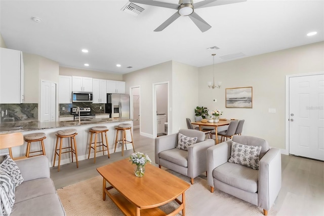 living room with sink, light hardwood / wood-style floors, and ceiling fan with notable chandelier