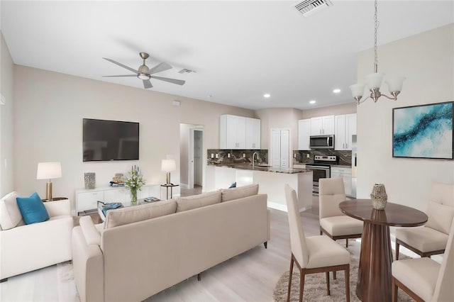 living room featuring light hardwood / wood-style flooring, ceiling fan with notable chandelier, and sink