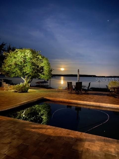 pool at dusk featuring a patio and a water view