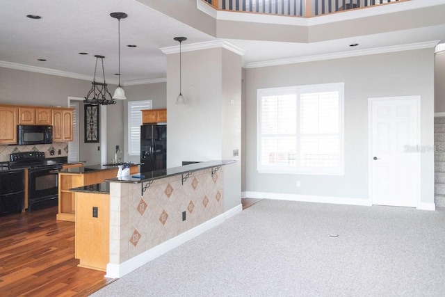 kitchen featuring a kitchen bar, crown molding, hanging light fixtures, and black appliances