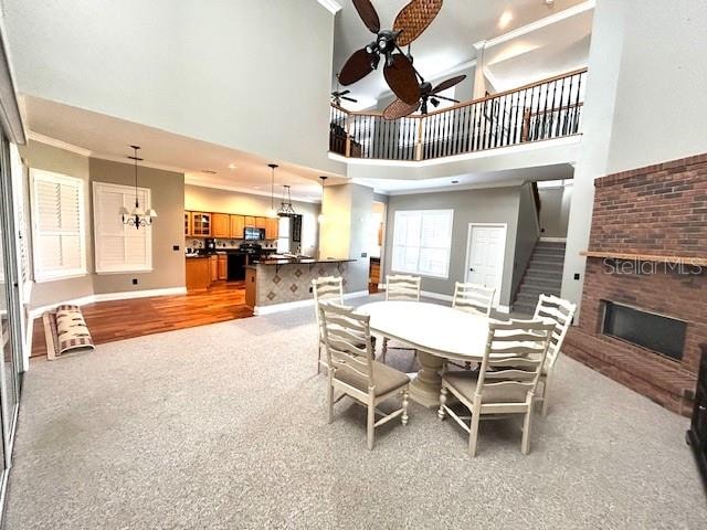 dining space with a towering ceiling, a brick fireplace, ornamental molding, ceiling fan with notable chandelier, and hardwood / wood-style floors