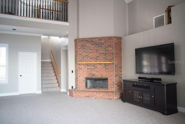 living room with carpet flooring, ornamental molding, a towering ceiling, and a brick fireplace