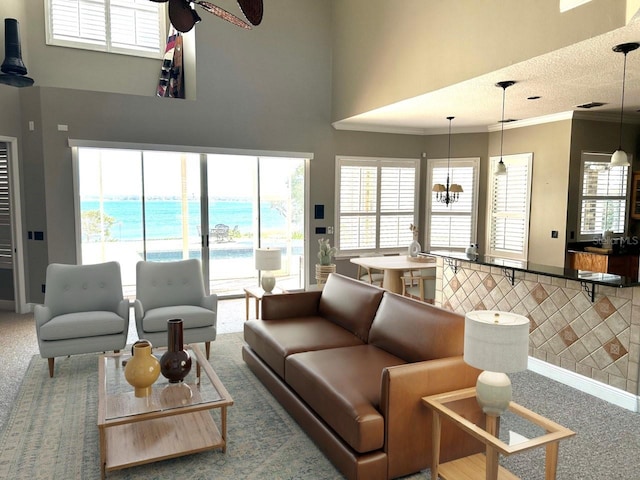 carpeted living room featuring a towering ceiling, ceiling fan with notable chandelier, a water view, and a wealth of natural light