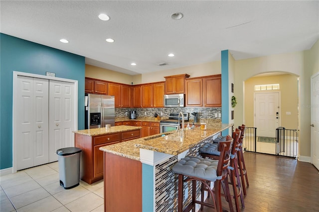 kitchen with a kitchen island, kitchen peninsula, stainless steel appliances, a breakfast bar, and light stone counters