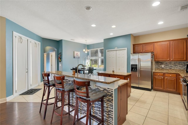 kitchen featuring a kitchen island with sink, a kitchen breakfast bar, stainless steel appliances, decorative light fixtures, and a textured ceiling