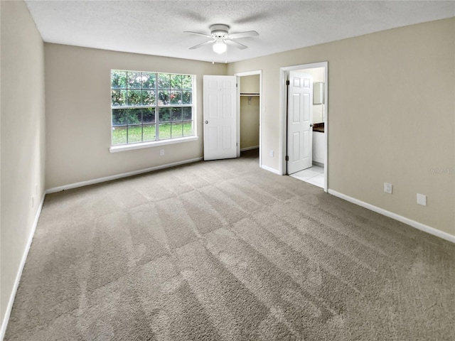 unfurnished bedroom featuring light carpet, ceiling fan, a textured ceiling, a walk in closet, and ensuite bath