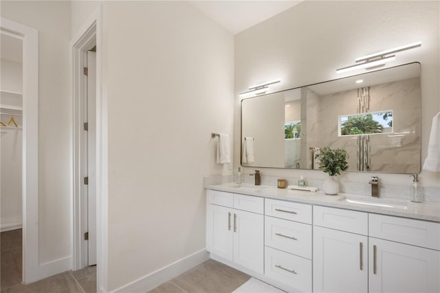 full bath featuring a sink, a walk in closet, baseboards, and double vanity