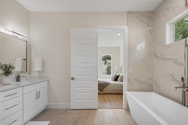 bathroom with plenty of natural light, a soaking tub, wood finished floors, and vanity