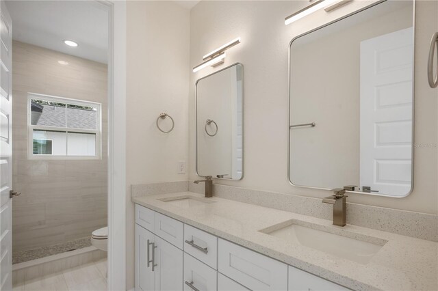 full bathroom with a tile shower, double vanity, toilet, and a sink