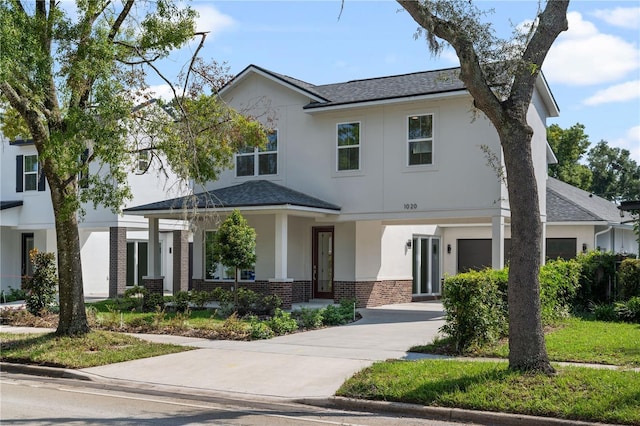 view of front of home featuring stucco siding, brick siding, roof with shingles, and concrete driveway