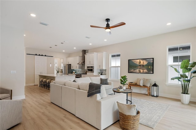 living room with recessed lighting, light wood-style flooring, a barn door, and ceiling fan