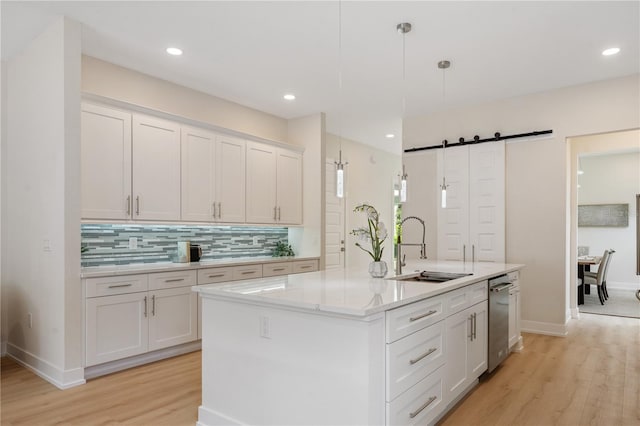 kitchen with tasteful backsplash, a barn door, light wood-style flooring, white cabinets, and a sink