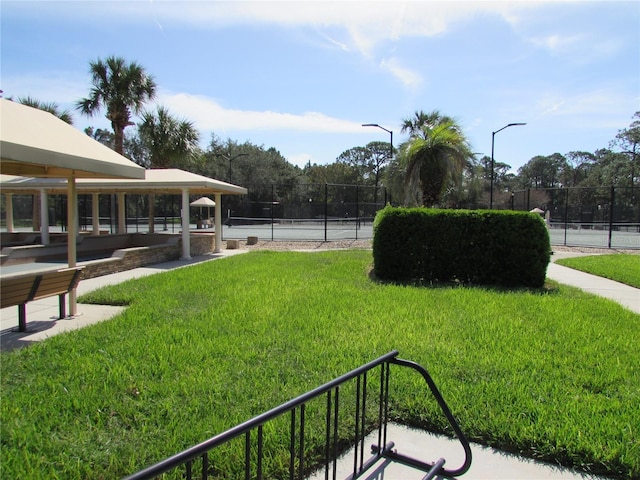 view of community featuring tennis court and a lawn