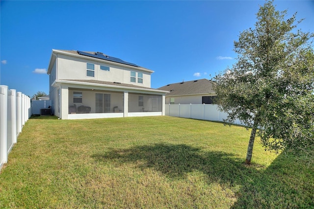 rear view of house featuring central air condition unit, solar panels, a lawn, and a sunroom