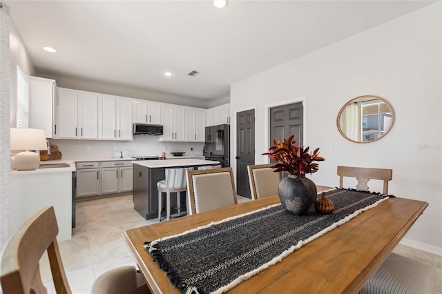 kitchen with a kitchen island, black fridge, a breakfast bar area, white cabinets, and light tile patterned floors