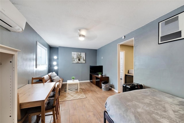 bedroom with a wall unit AC, light wood-type flooring, and ceiling fan