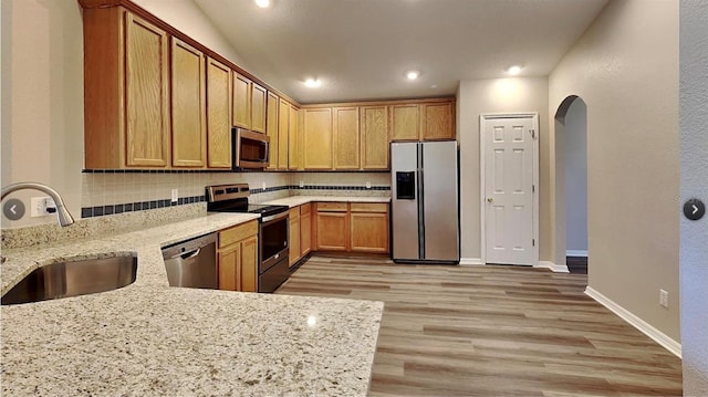 kitchen featuring stainless steel appliances, light stone countertops, sink, and kitchen peninsula