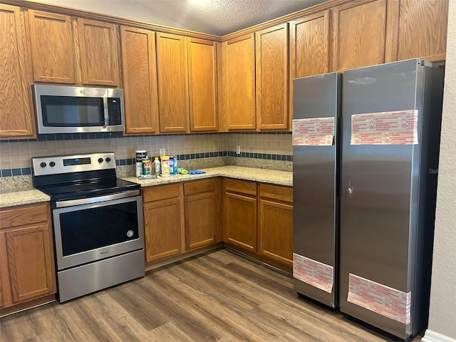 kitchen with appliances with stainless steel finishes, light stone counters, and wood-type flooring