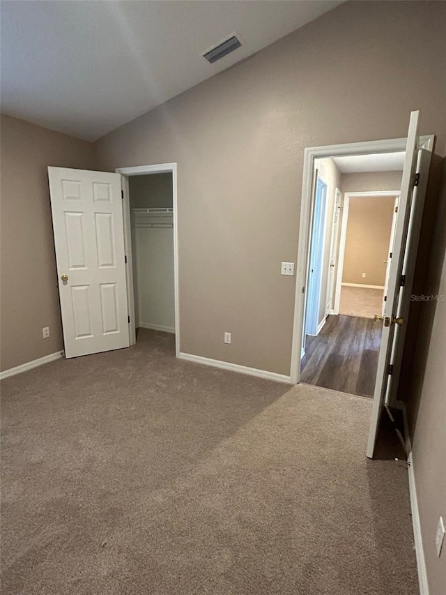 unfurnished bedroom featuring a closet, lofted ceiling, and dark colored carpet