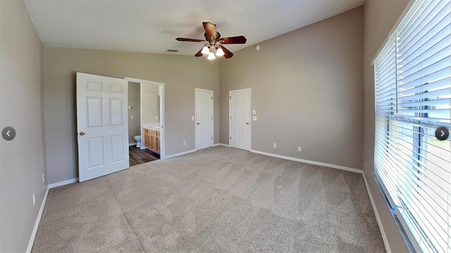 unfurnished bedroom with lofted ceiling, ensuite bathroom, carpet flooring, and ceiling fan