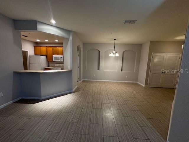 kitchen featuring kitchen peninsula, hardwood / wood-style floors, a notable chandelier, decorative light fixtures, and white appliances