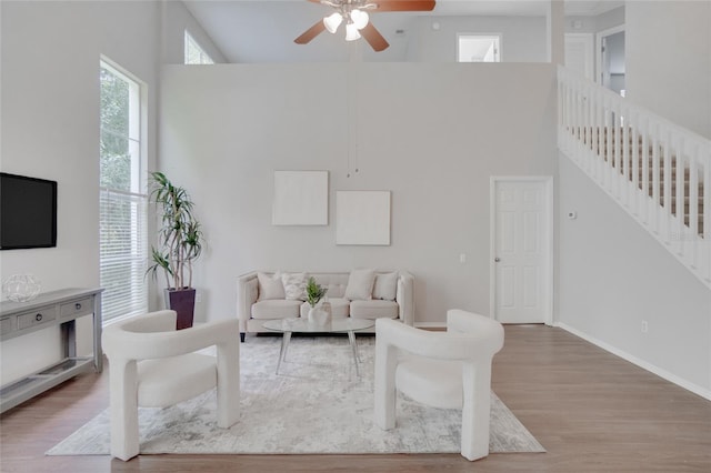 living room featuring ceiling fan, a towering ceiling, and hardwood / wood-style floors