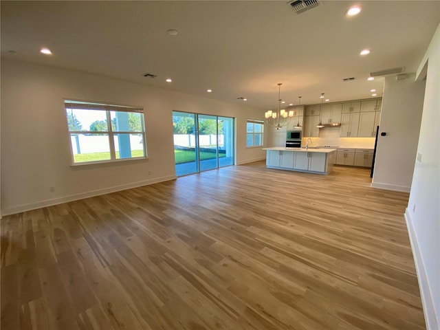 unfurnished living room featuring sink, light hardwood / wood-style flooring, and a notable chandelier