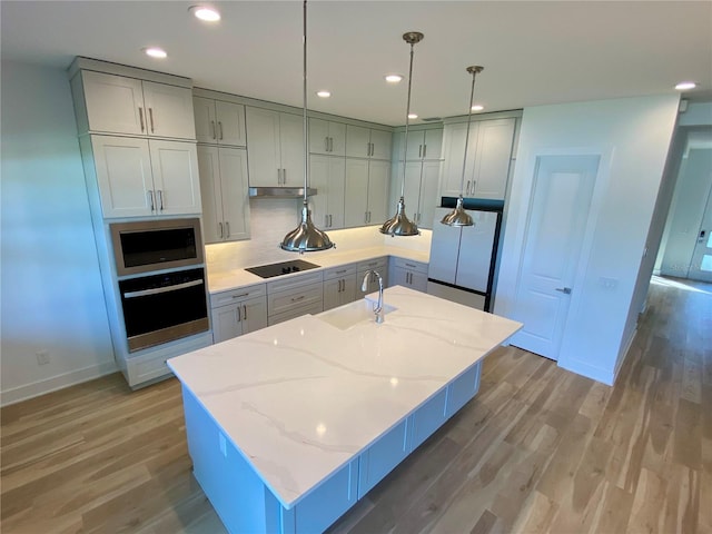 kitchen featuring a kitchen island with sink, stainless steel appliances, sink, light wood-type flooring, and light stone counters