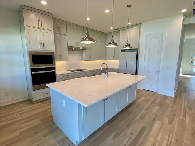 kitchen with sink, a kitchen island with sink, light stone counters, and stainless steel appliances