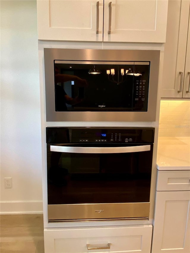 details with appliances with stainless steel finishes, white cabinets, hardwood / wood-style flooring, and light stone counters