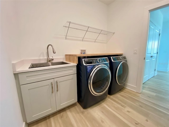 laundry area with light hardwood / wood-style floors, cabinets, sink, and washing machine and clothes dryer