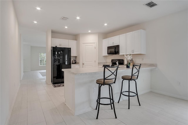 kitchen featuring black appliances, kitchen peninsula, a kitchen bar, and white cabinets