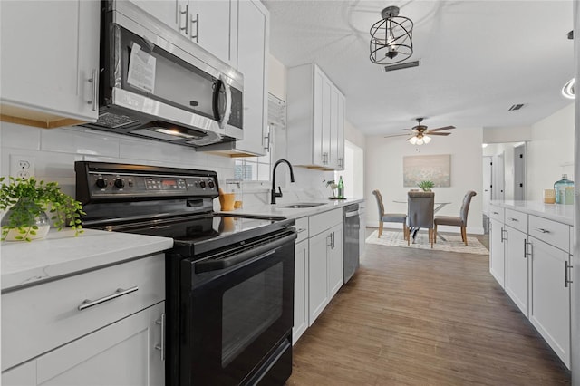 kitchen featuring appliances with stainless steel finishes, sink, dark hardwood / wood-style flooring, white cabinetry, and pendant lighting