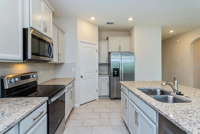 kitchen featuring sink, white cabinets, light tile patterned floors, appliances with stainless steel finishes, and light stone counters