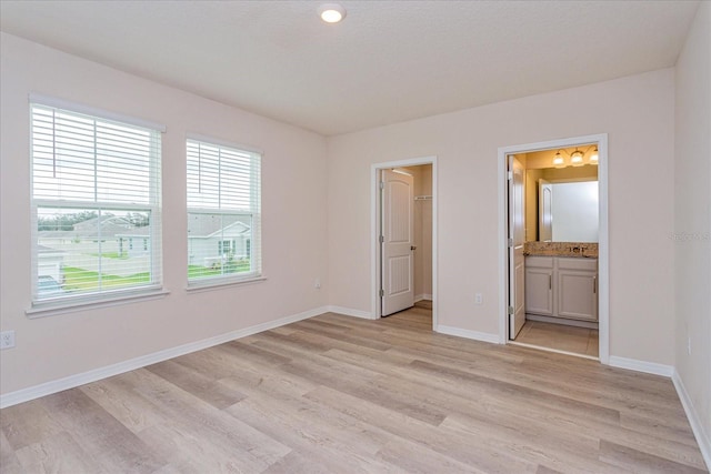 unfurnished bedroom featuring a spacious closet, ensuite bathroom, and light wood-type flooring