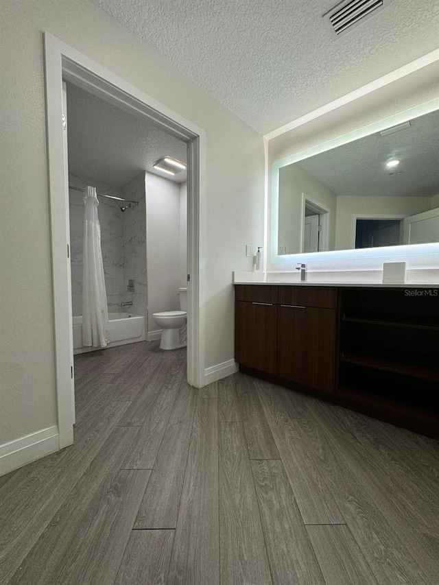 full bathroom featuring a textured ceiling, hardwood / wood-style floors, shower / bath combination with curtain, toilet, and vanity