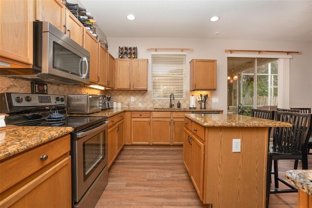 kitchen with a kitchen breakfast bar, light stone counters, stainless steel appliances, sink, and a center island