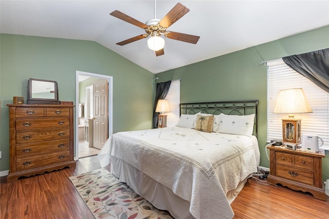 bedroom featuring light wood-type flooring, ensuite bath, ceiling fan, and vaulted ceiling